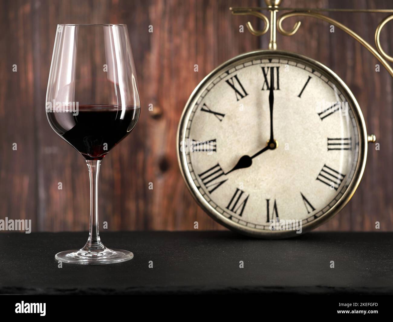 Verre de vin rouge avec horloge antique sur fond de bois, image de concept pour le dîner ou l'alcoolisme le soir après le travail Banque D'Images