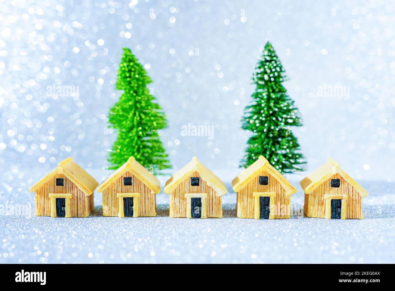 Rangée de maisons miniatures placées devant deux arbres de Noël sur fond étincelant. Banque D'Images