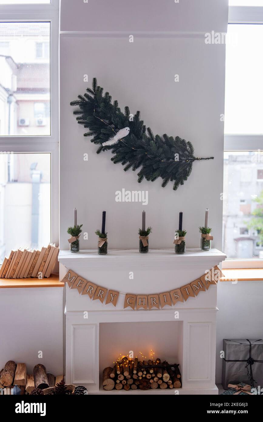 Décoration de Noël minimaliste près de la cheminée. Style scandinave rustique. Guirlande d'épinette à feuilles persistantes avec oiseau pend sur le mur blanc, han Banque D'Images
