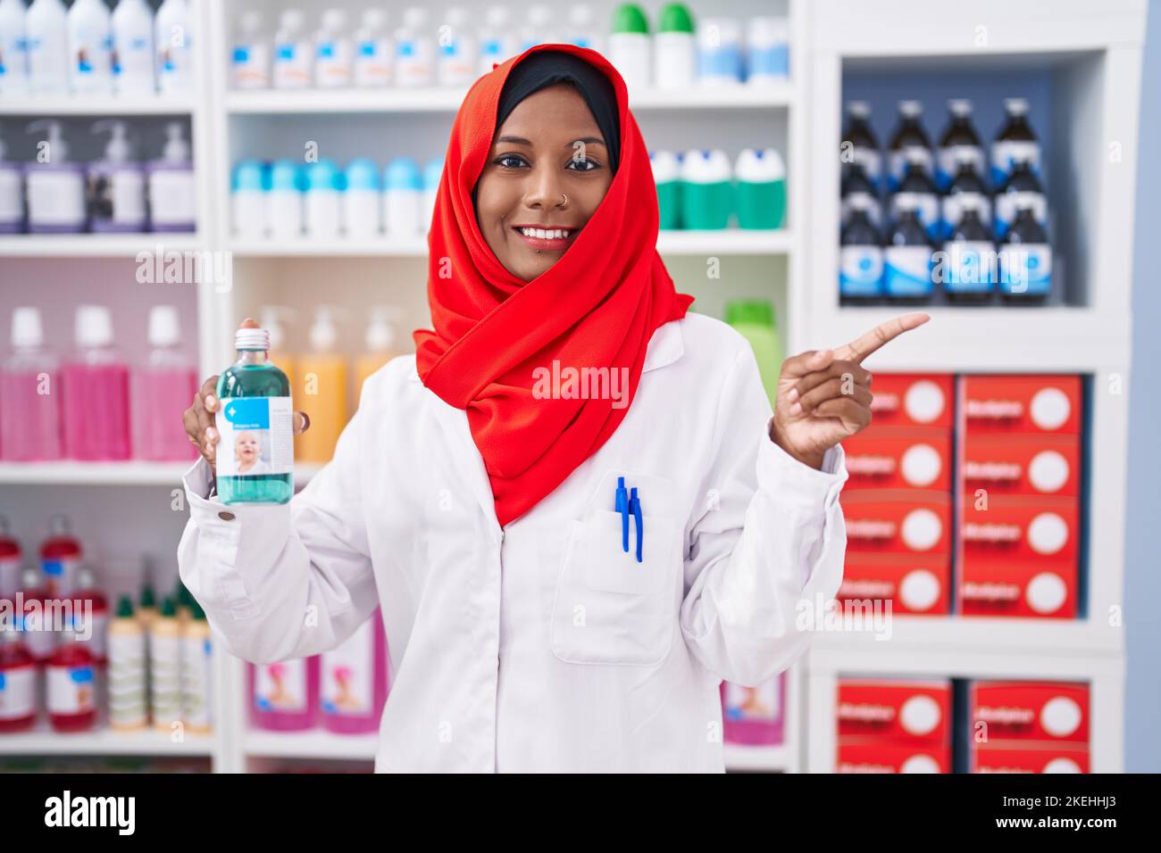 Jeune femme arabe travaillant à pharmacie pharmacie pharmacie pharmacie tenue sirop sourire heureux pointant avec la main et le doigt sur le côté Banque D'Images