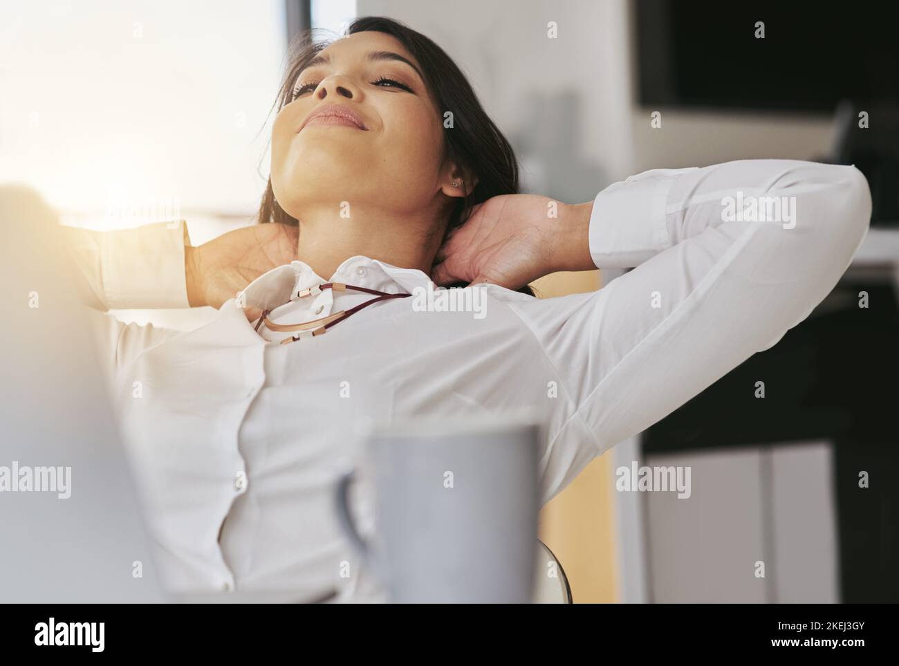 Retrouver son succès. Une jeune femme d'affaires content assise dans son bureau avec ses mains derrière sa tête. Banque D'Images