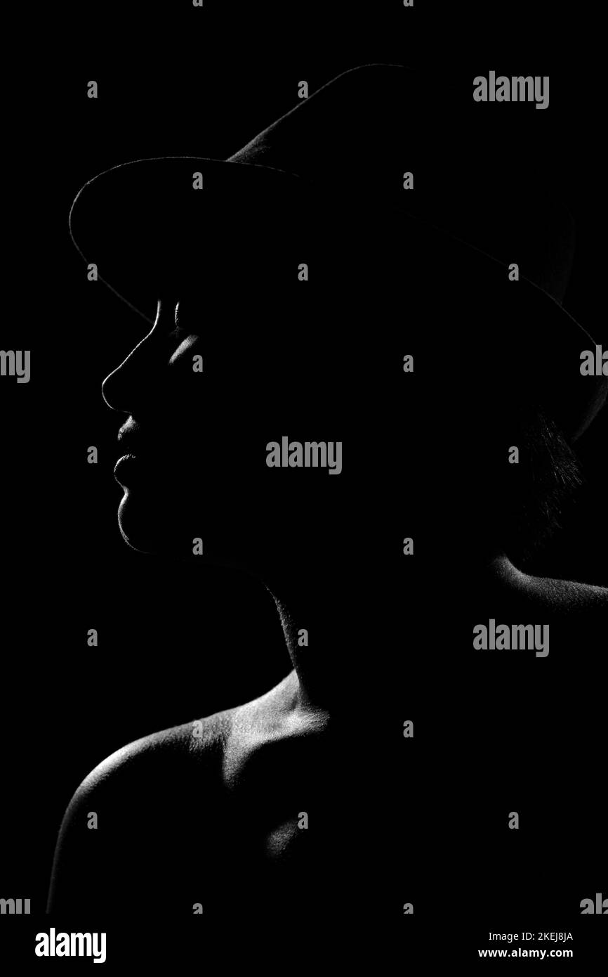 Profil de silhouette d'une jeune femme magnifique sur un fond sombre. Fille avec chapeau et rebord de lumière autour d'elle. monochrome Banque D'Images