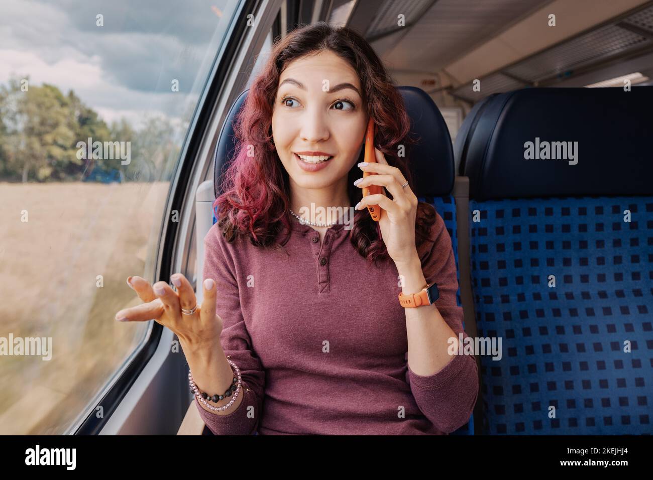 Une fille asiatique parle amblement avec un client ou un ami au téléphone lors d'un voyage dans un pays à bord d'un train à grande vitesse moderne Banque D'Images