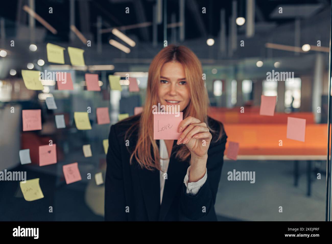 Femme d'affaires souriante montrant des notes adhésives avec des phrases de motivation pendant qu'elle se trouve au bureau Banque D'Images