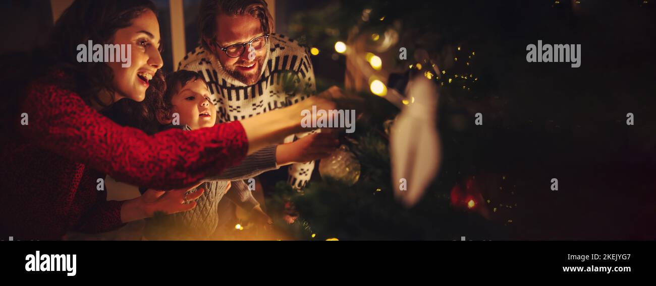 Famille de trois sapins préparant les fêtes de la veille de Noël à la maison.Famille décorant arbre de Noël ensemble à la maison. Banque D'Images