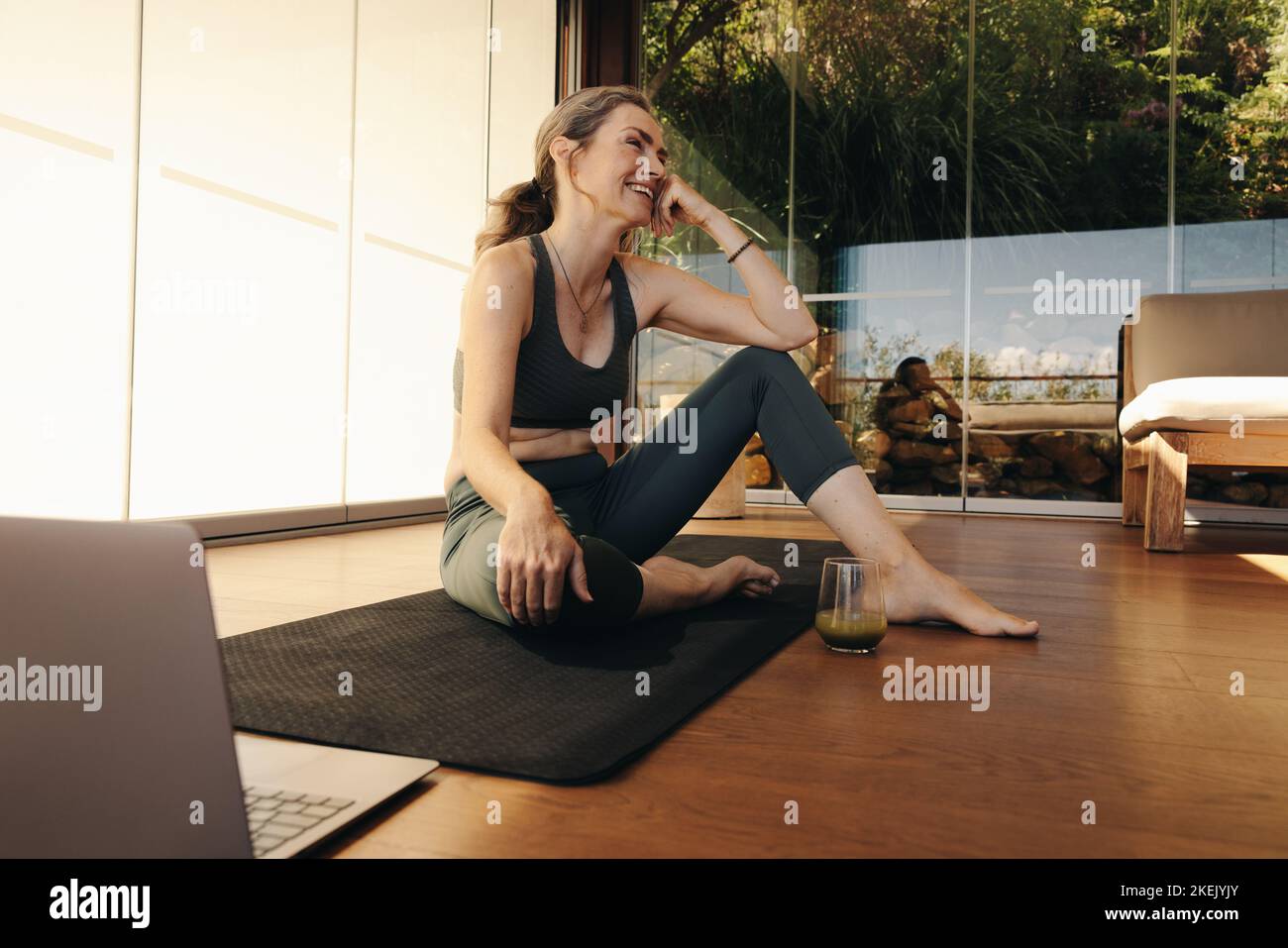 Bonne femme âgée souriant assis devant un ordinateur portable sur un tapis d'exercice. Femme mature prenant une pause d'un cours de yoga à la maison. L'elde gaie Banque D'Images