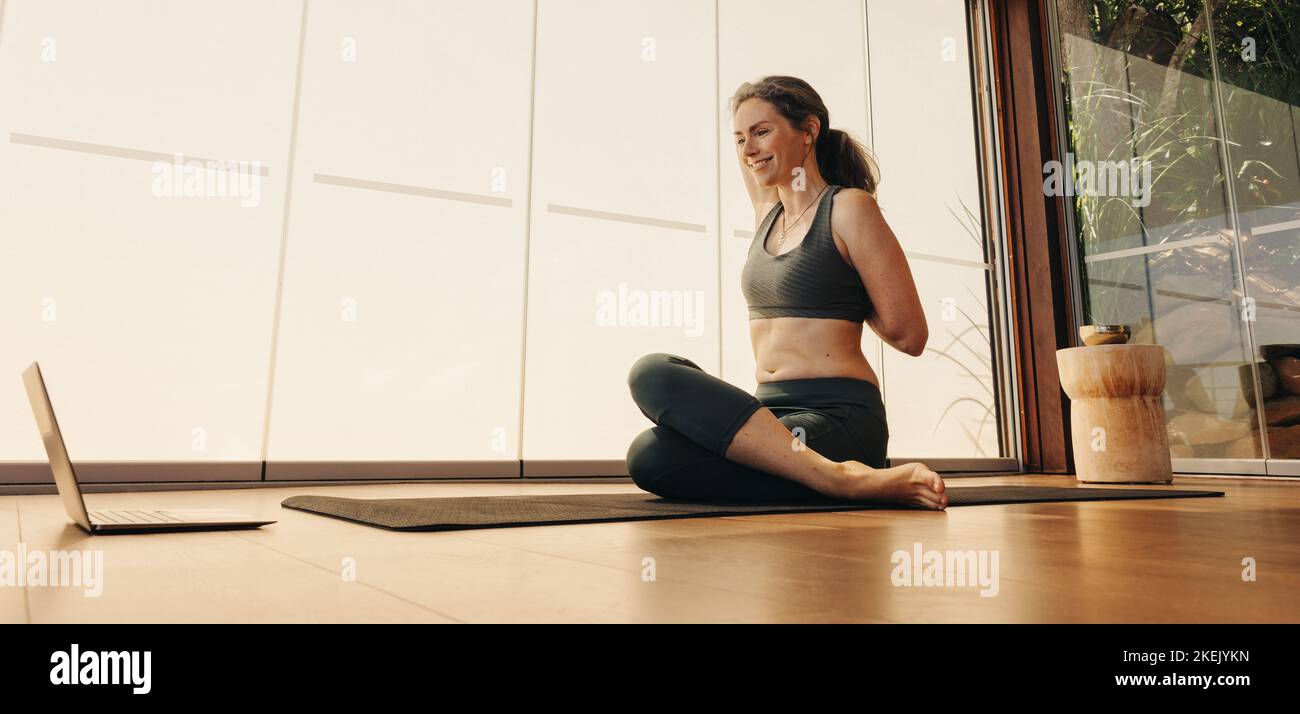 Bonne femme âgée faisant une pose de tête de vache pendant un cours de yoga en ligne à la maison. Femme mûre souriante pratiquant un asana étirant sur un tapis de yoga. Femme Banque D'Images