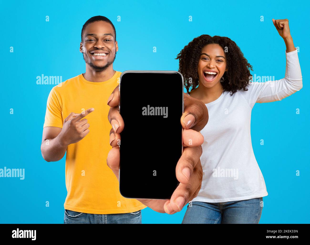 Heureux émotionnel millénaire couple afro-américain célébrer la victoire avec les mains gestuelle, montrer grand téléphone avec écran vide Banque D'Images