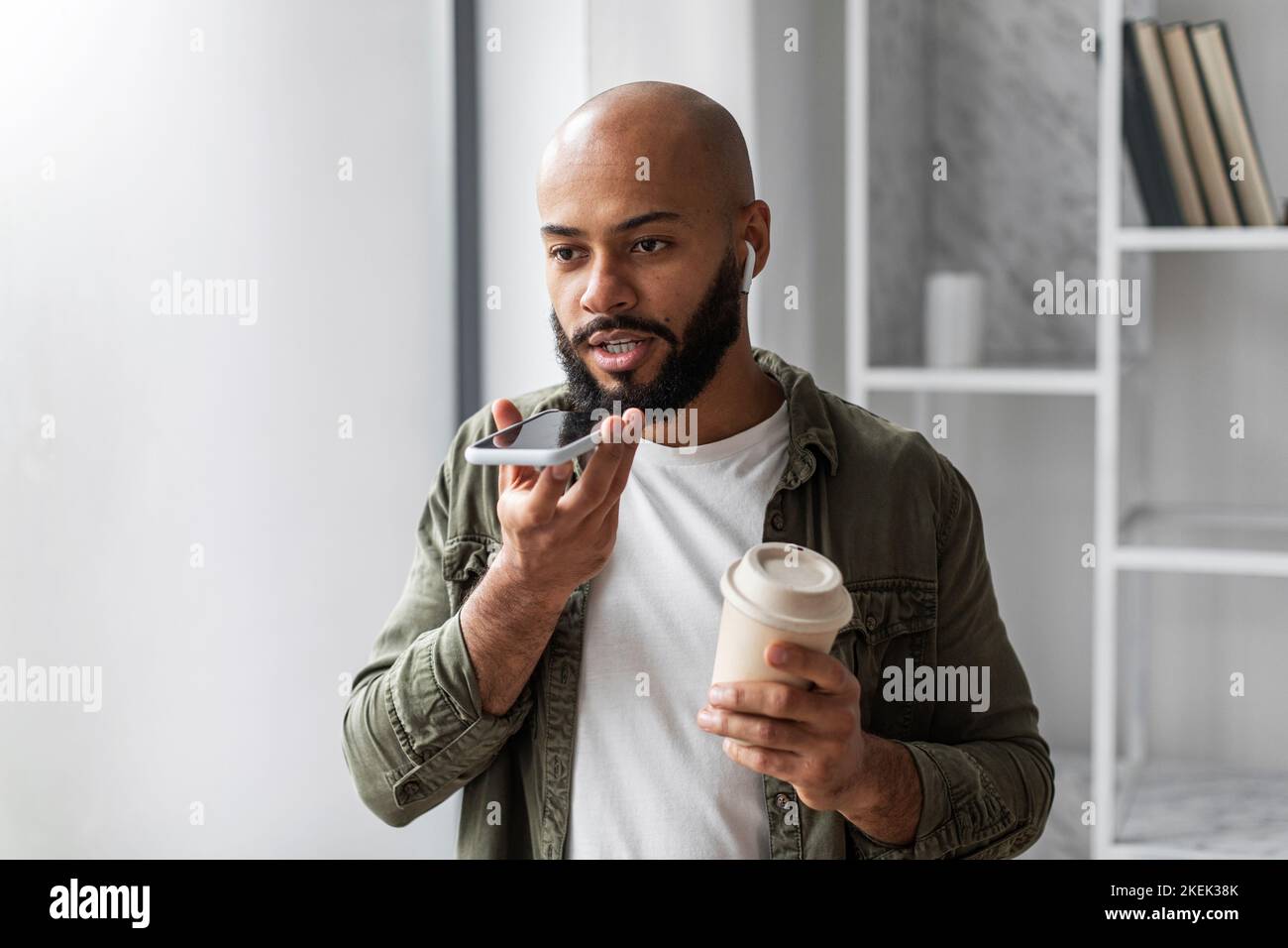 Latino-américain enregistrant un message vocal sur smartphone et buvant un café dans une tasse à emporter, en profitant des technologies modernes Banque D'Images