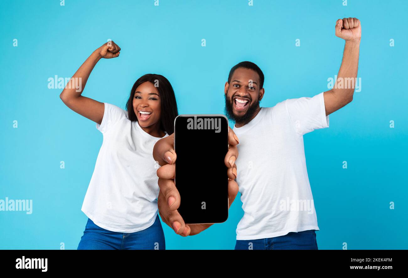 Un couple afro-américain millénaire satisfait et émotionnel célèbre la victoire avec ses mains gestuelles, montrez votre smartphone Banque D'Images