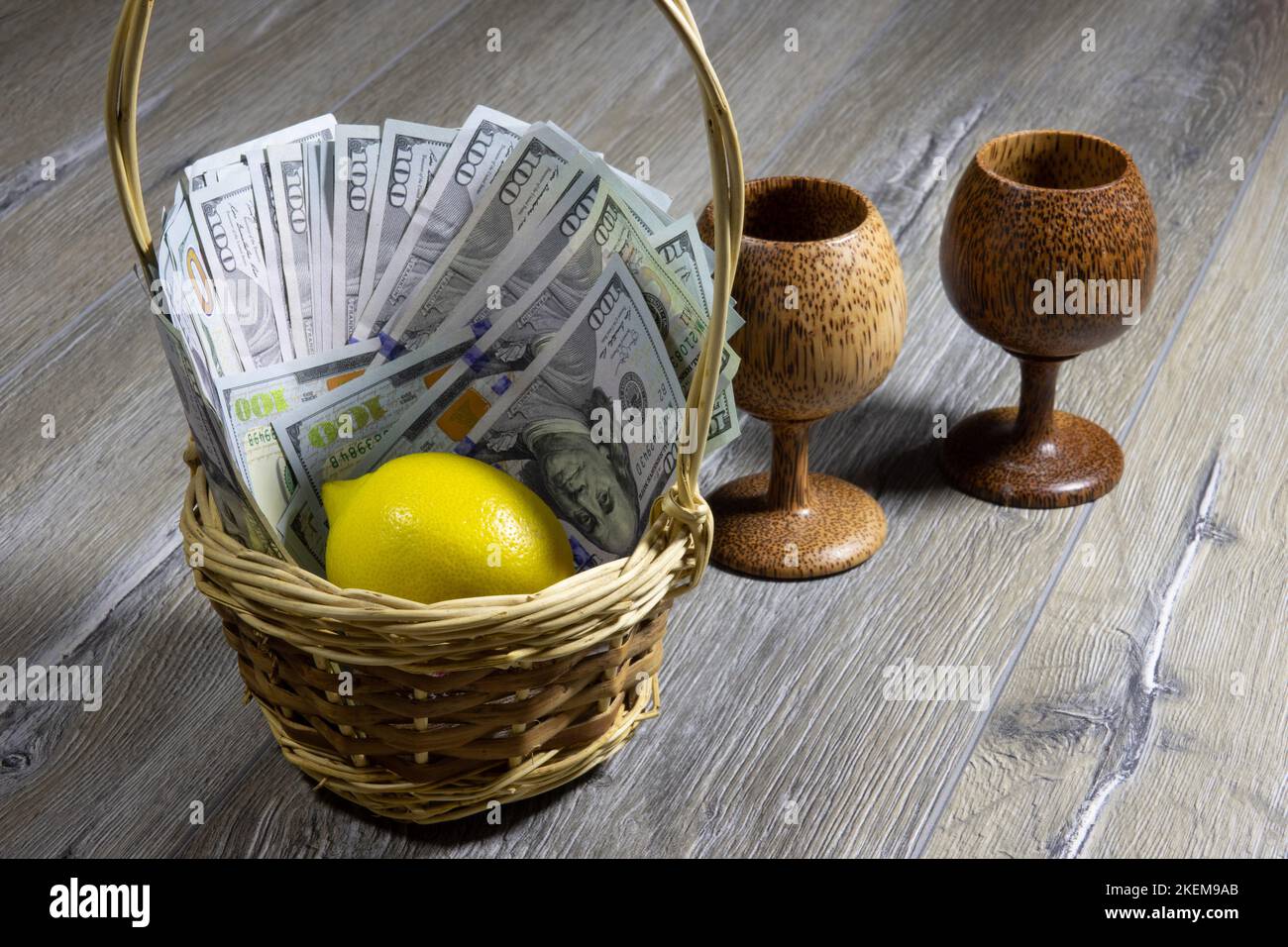 Panier en osier avec billets de cent dollars américains et citron à l'intérieur sur une table en bois gris avec deux gobelets en bois. Banque et finan Banque D'Images