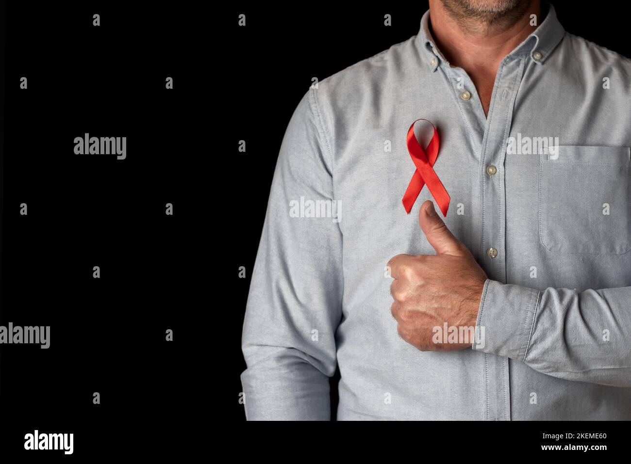 Un homme portant un ruban rouge de la Journée mondiale du sida sur sa poitrine avec son pouce vers le haut pour soutenir toutes les personnes séropositives. Combattre la maladie et le vih viru Banque D'Images
