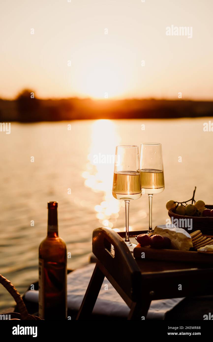 Coucher de soleil incroyable sur le lac, vin blanc, gâteau aux fruits, pommes, raisins, fromage brie, biscuits. Pique-nique esthétique d'automne. Banque D'Images