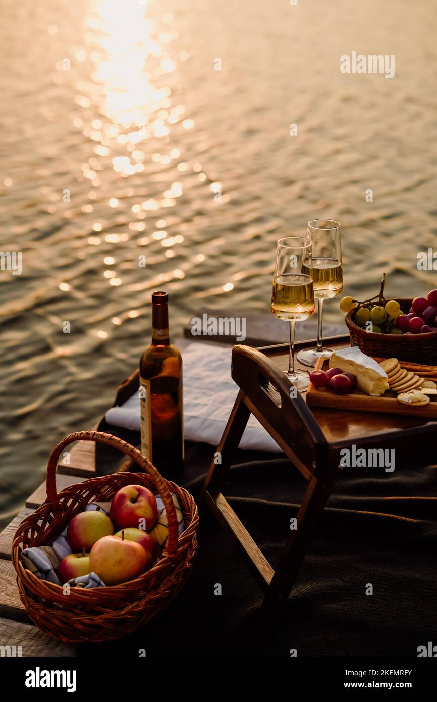Coucher de soleil incroyable sur le lac, vin blanc, gâteau aux fruits, pommes, raisins, fromage brie, biscuits. Pique-nique esthétique d'automne. Banque D'Images