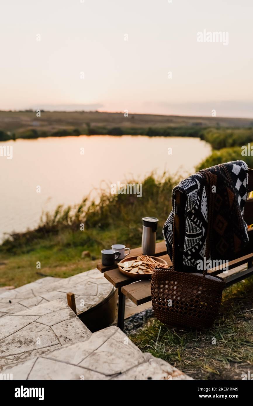 Coucher de soleil incroyable sur le lac, café, romance. Pique-nique esthétique d'automne. Une belle couverture sur un banc en face du lac. Pique-nique esthétique à l'extérieur. Banque D'Images