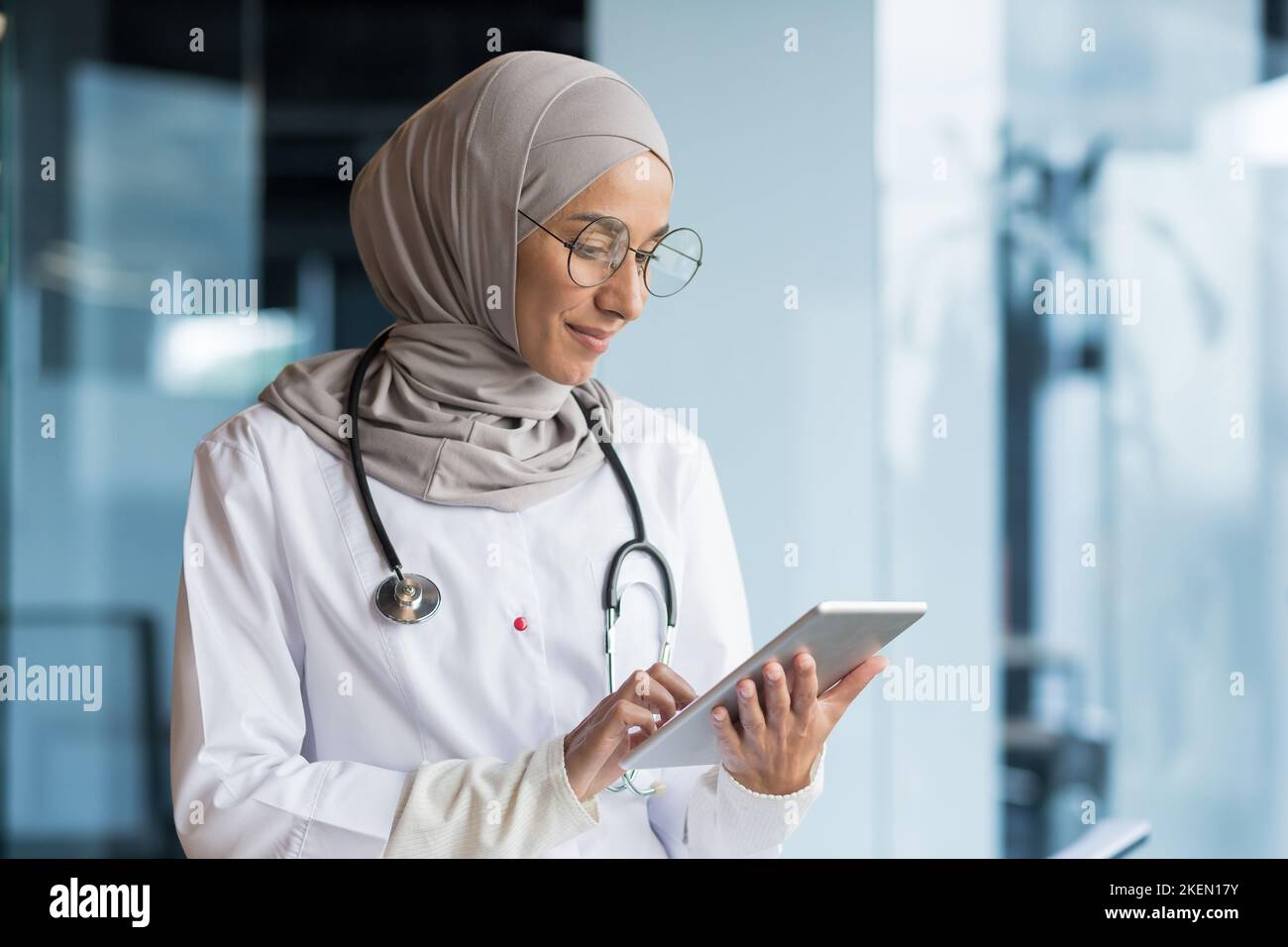 Gros plan. Une jeune femme arabe, un médecin musulman est debout à l'hôpital dans un bureau dans un hijab et avec un stéthoscope. Elle tient une tablette dans ses mains, se concentre sur le travail, la dactylographie. Banque D'Images