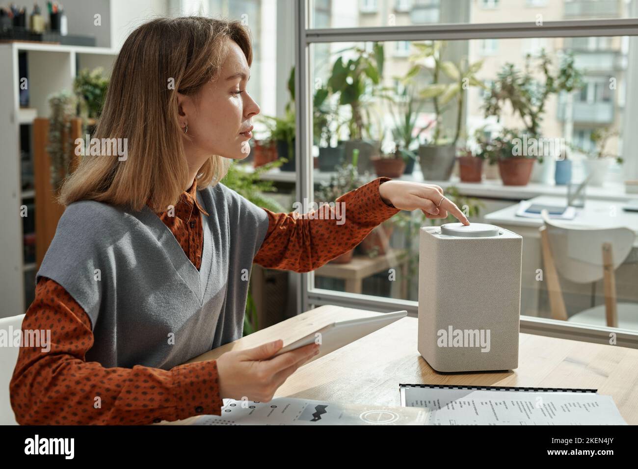 Jeune femme qui connecte une enceinte intelligente à une tablette pc tout en travaillant dans un bureau moderne avec des plantes vertes Banque D'Images