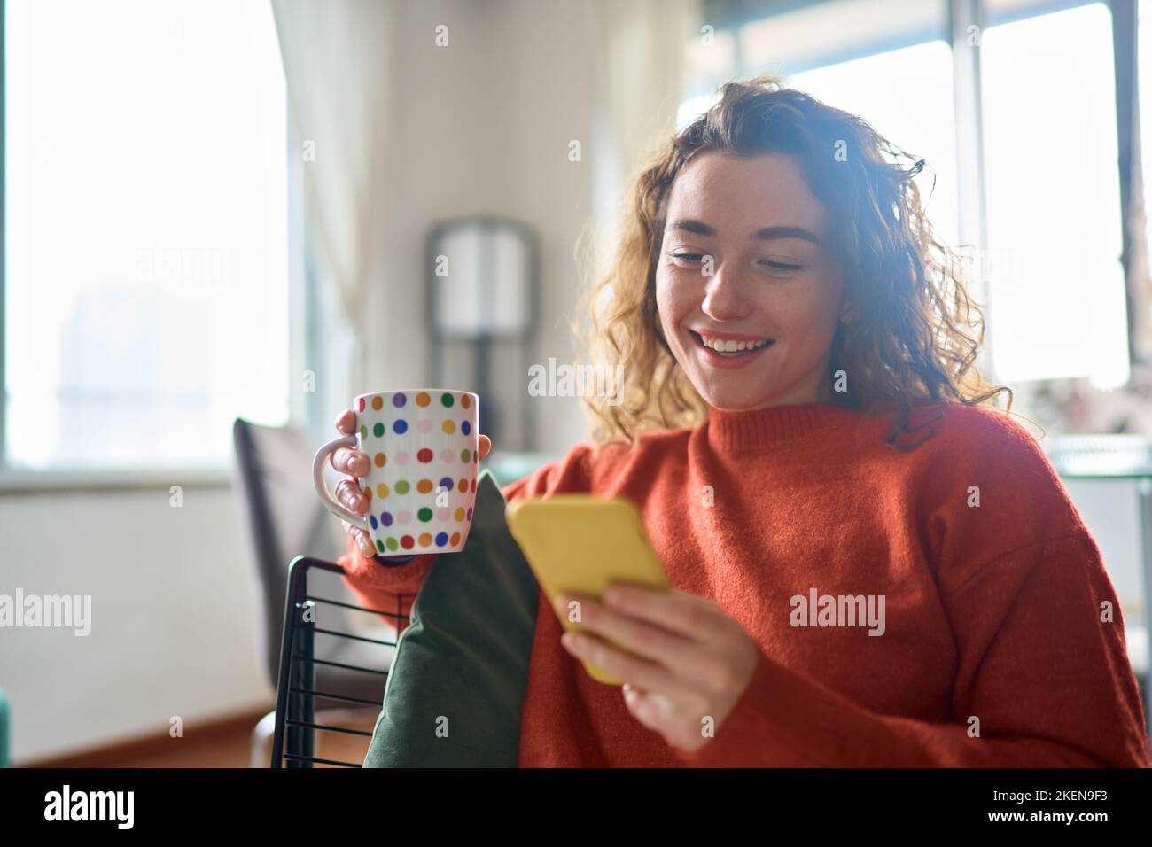 Jeune femme heureuse utilisant un téléphone mobile boire du café se détendre à la maison. Banque D'Images