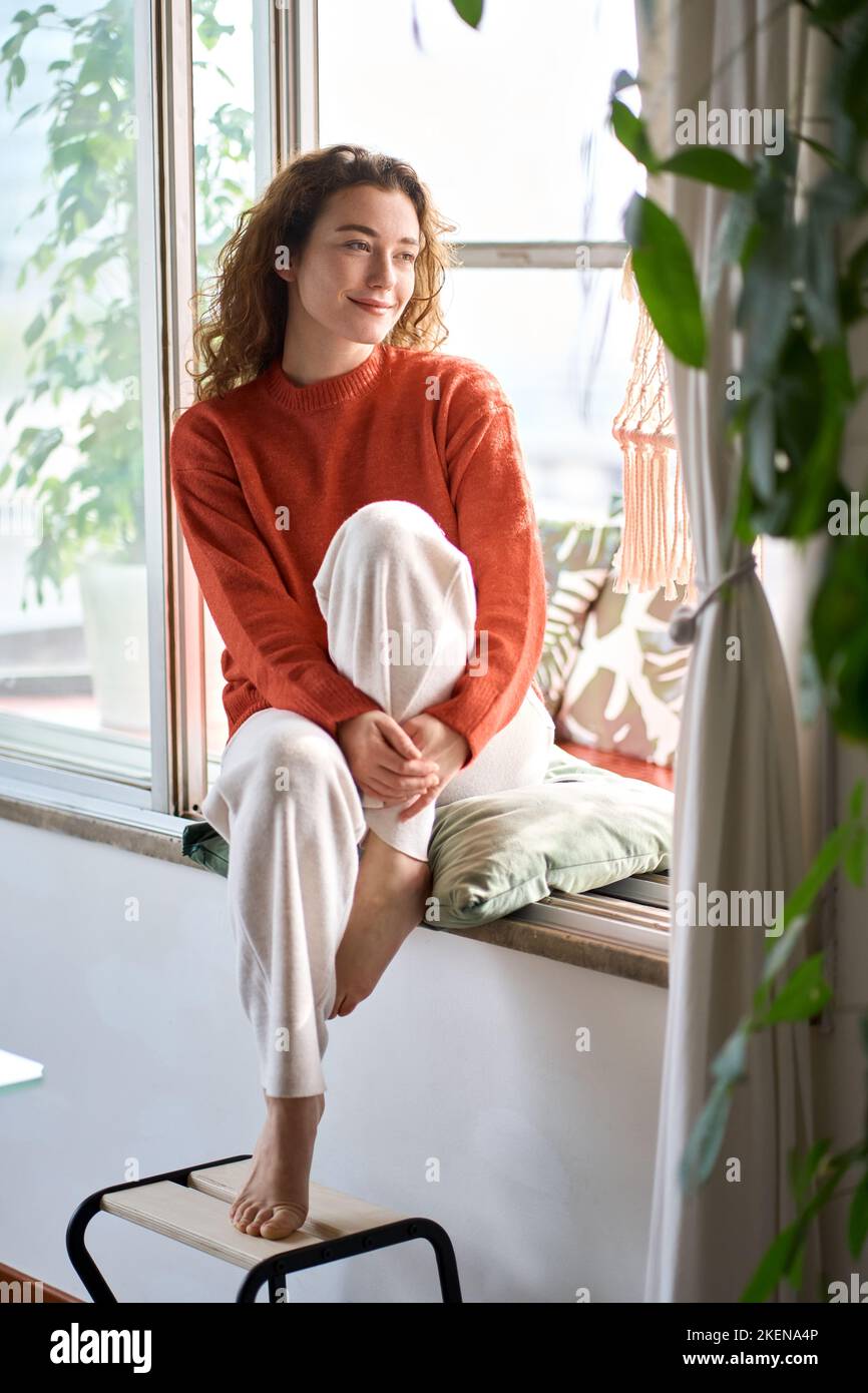 Bonne sereine jeune femme assise reposant à la maison regardant par la fenêtre. Banque D'Images