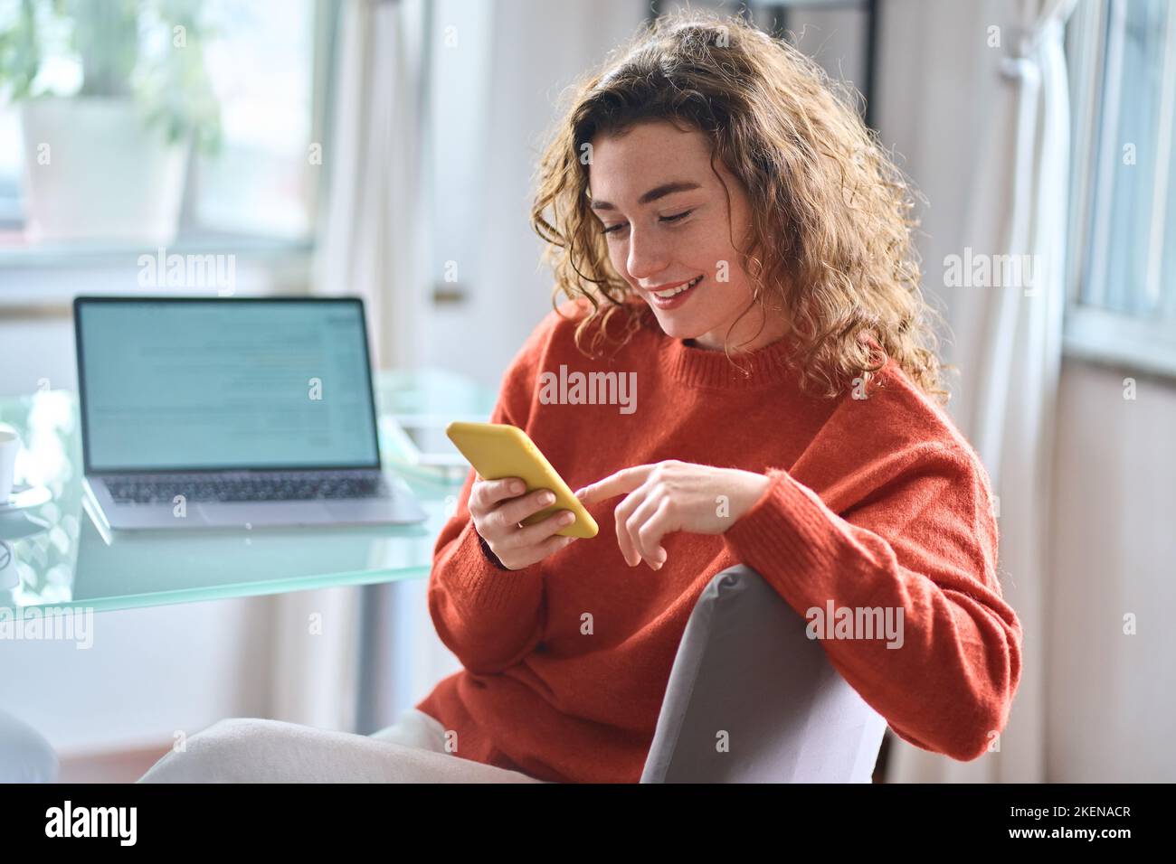 Jeune femme souriante tenant un téléphone portable à la maison avec un smartphone. Banque D'Images