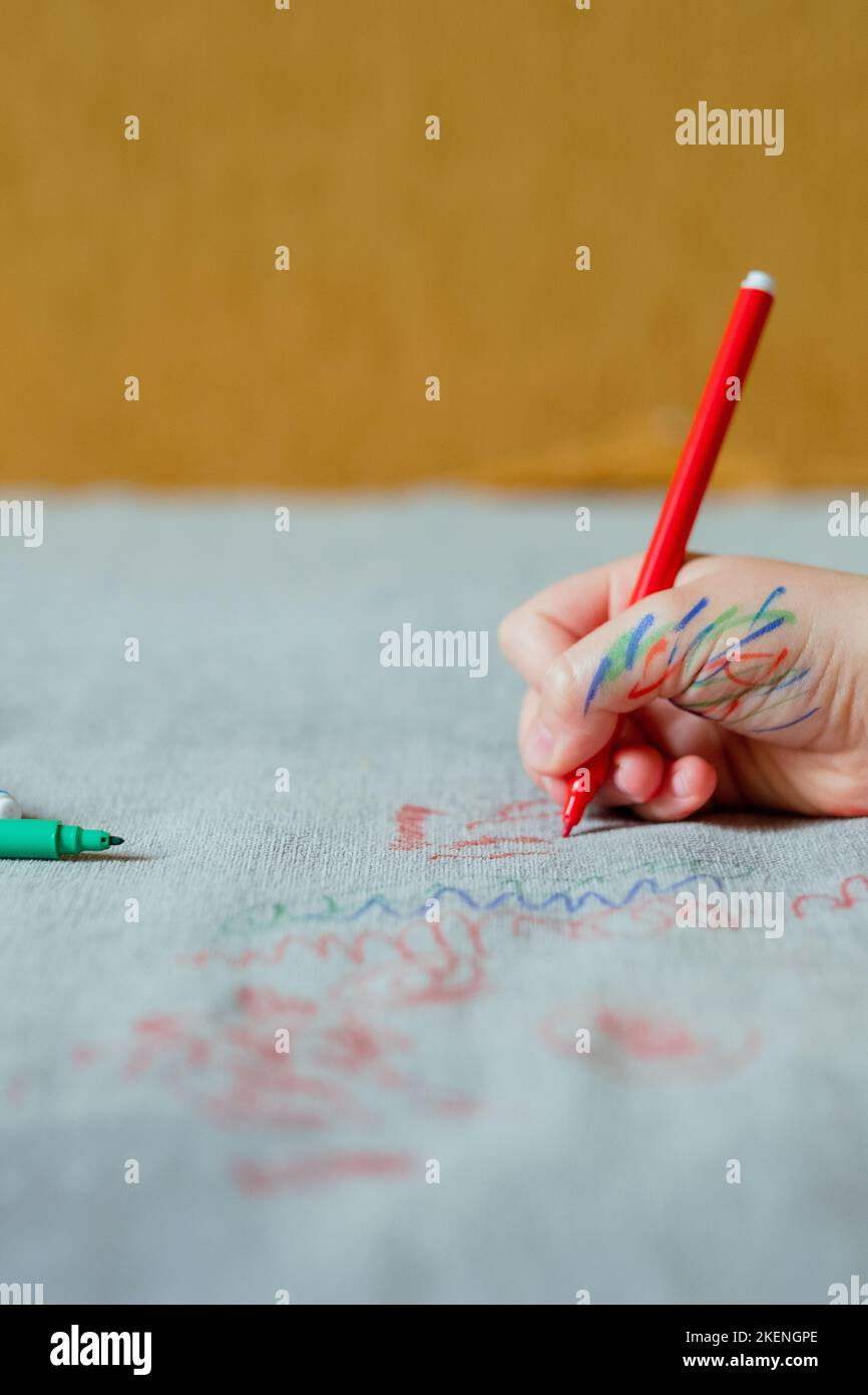 Un enfant est taché d'encre à la main, en dessinant avec un marqueur rouge sur la sellerie du canapé. Tissus de mobilier. Concept de nettoyage Banque D'Images