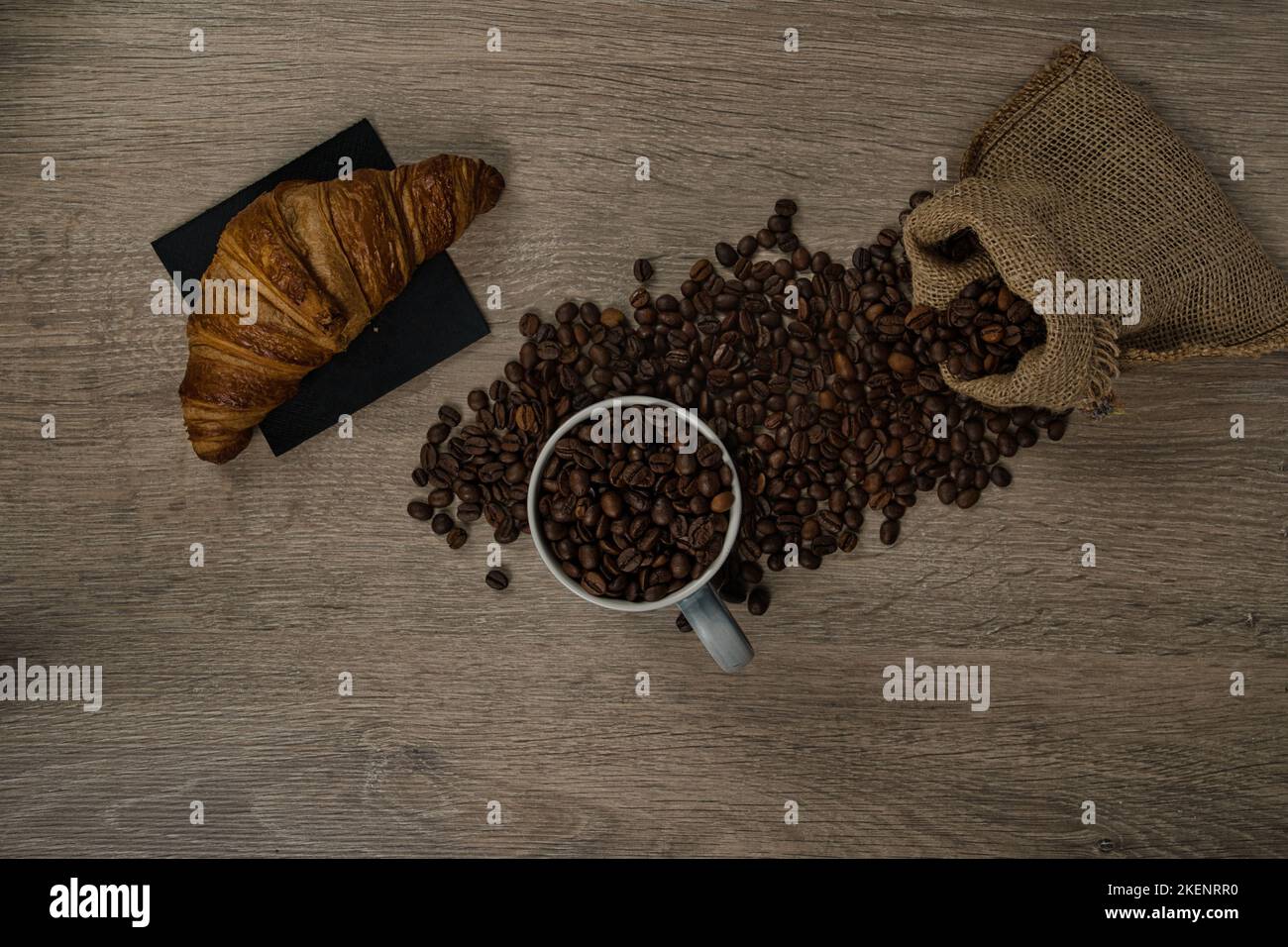 Vue de dessus des grains de café torréfiés bruns déversés sur une table avec une tasse de café et un biscuit, image Banque D'Images