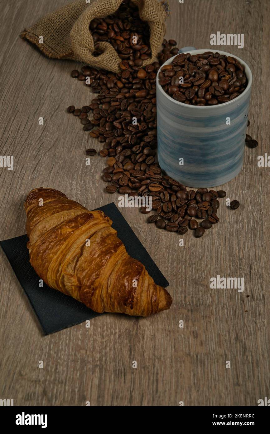 Vue de dessus des grains de café torréfiés bruns déversés sur une table avec une tasse de café et un biscuit, image Banque D'Images