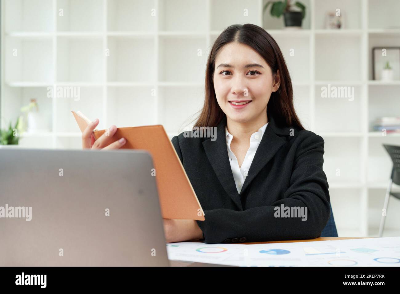 Portrait d'une belle femme d'affaires asiatique en costume habillé se trouve à son bureau avec un ordinateur portable et un ordinateur portable dans le bureau Banque D'Images