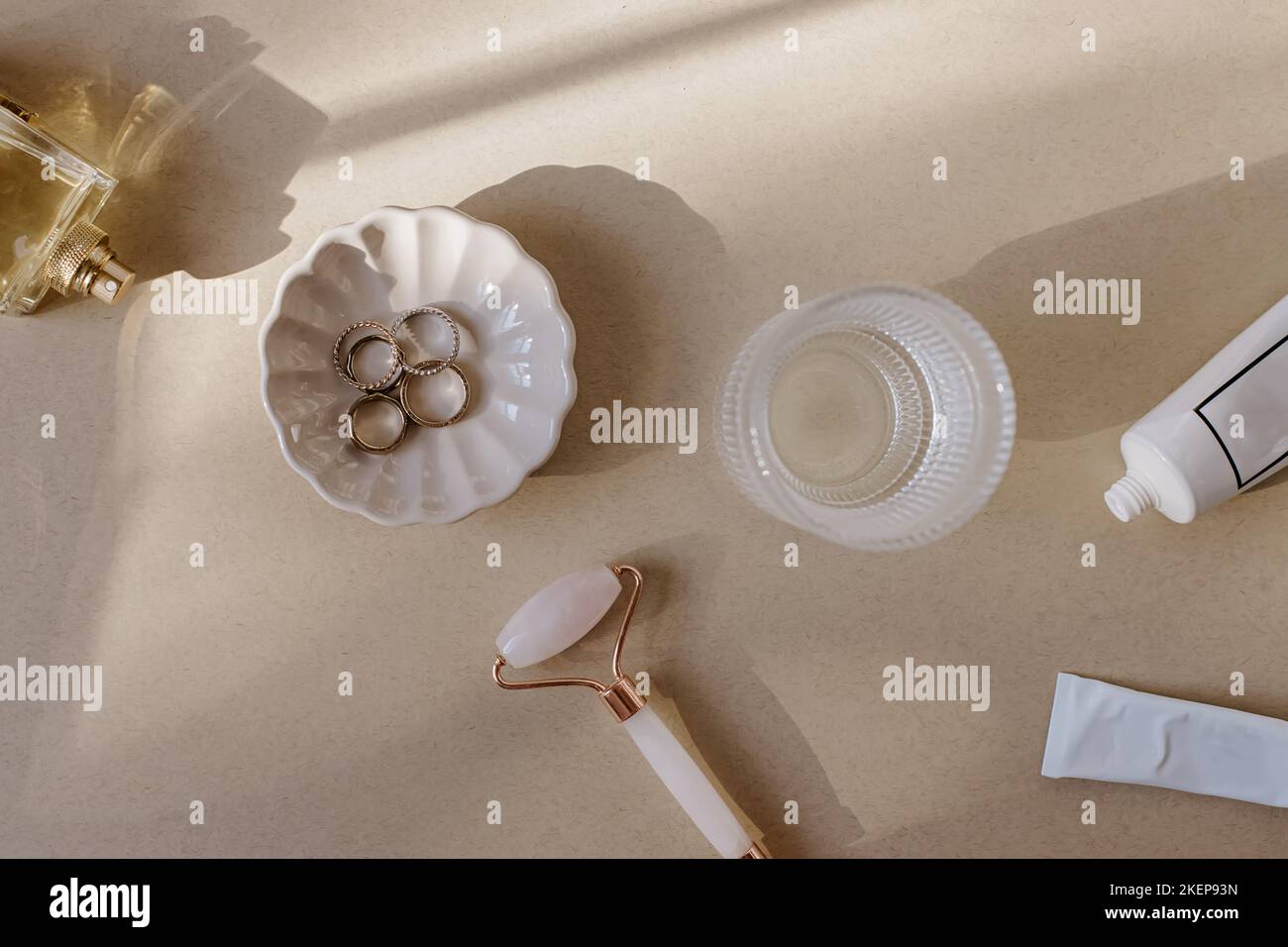 Outils et accessoires pour femme sur la table beige. Cosmétiques, rouleau de jade, eau, anneaux. Articles d'auto-soin Banque D'Images