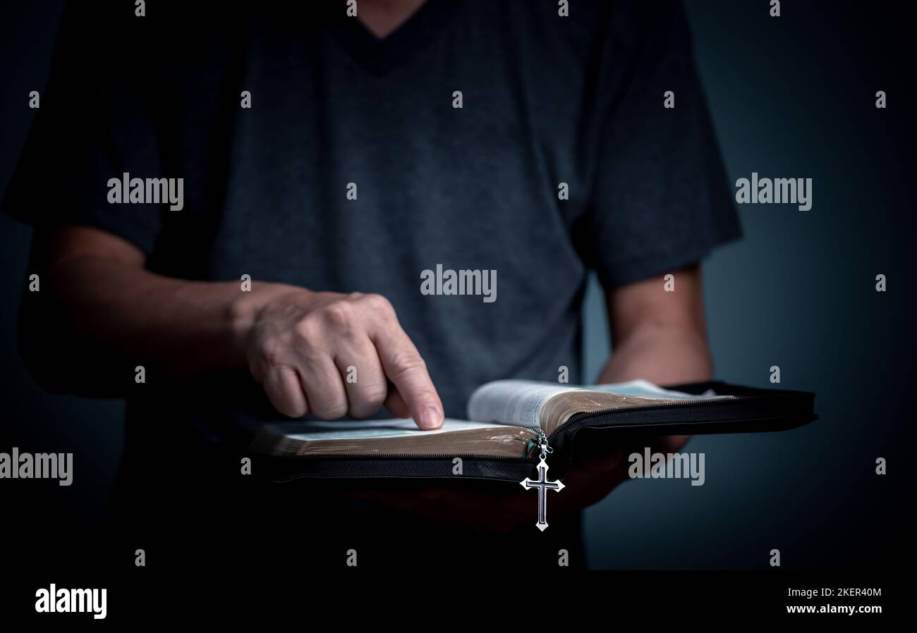 Jeune homme lisant la Sainte Bible et pointant sur la parole avec collier de croix en police de caractères du livre. Banque D'Images