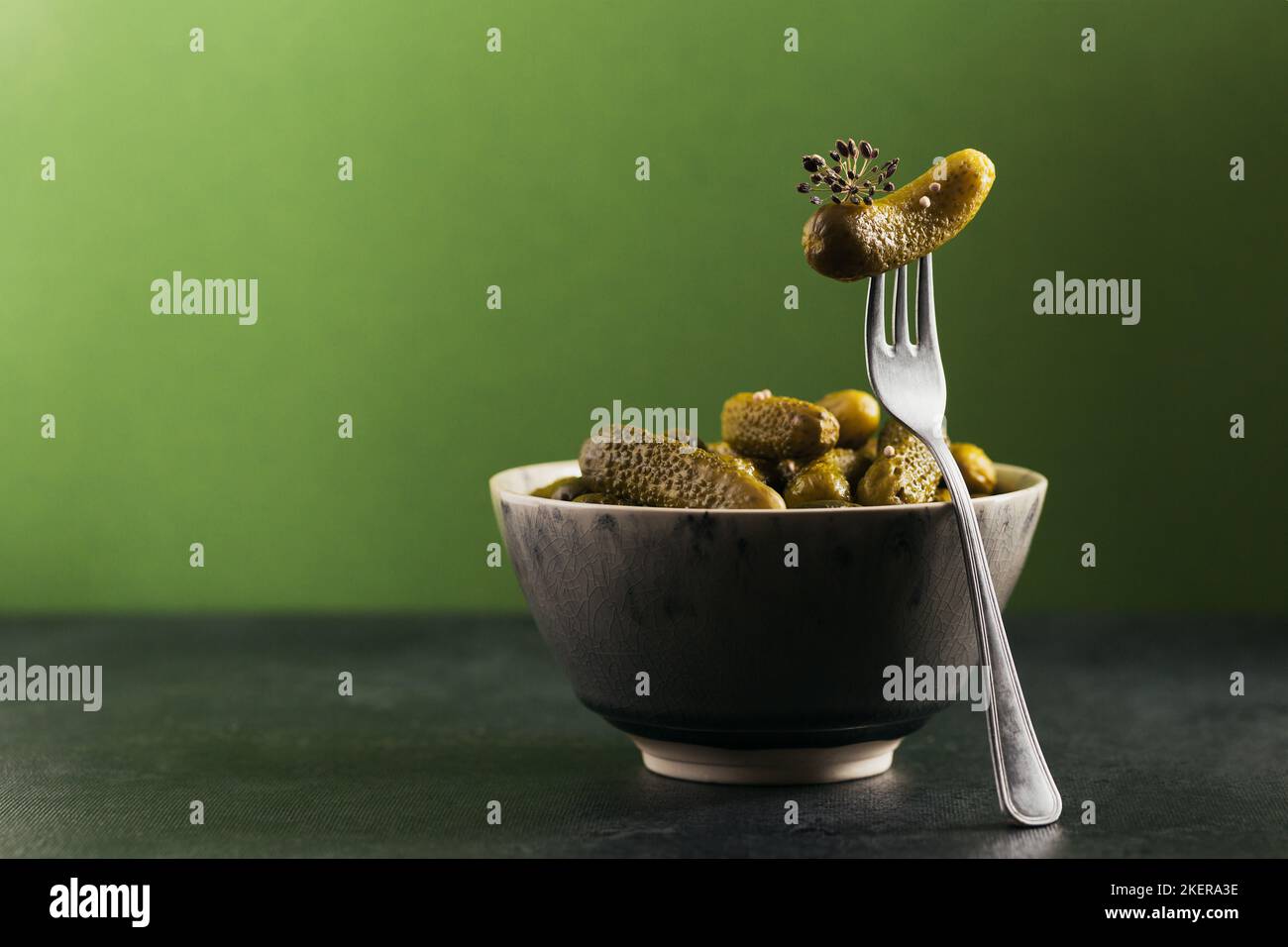 Cornichons, concombre mariné sur une fourchette, bol de légumes marinés sur fond vert. Cuisine propre, concept végétarien Banque D'Images