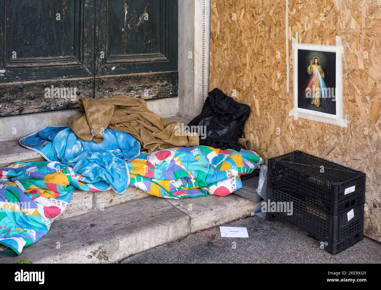 Sans abri à Rome. Un sans-abri qui se couche dans une porte d'entrée sur une rue de Rome avec une icône de Jusus accrochée au mur pour le regarder par-dessus lui. Rome. Latium, IT Banque D'Images