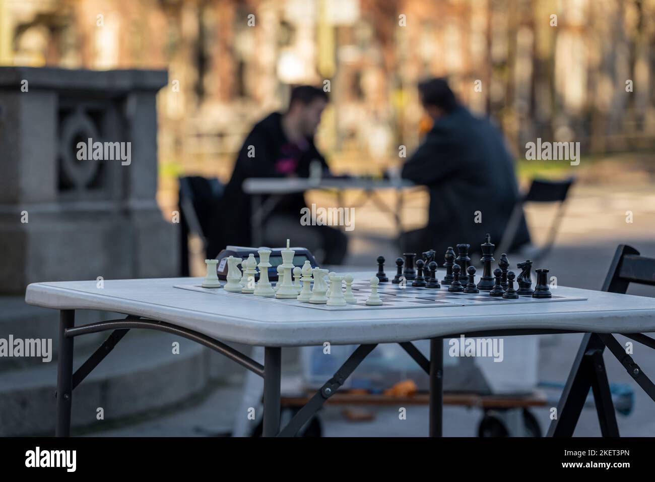 Jeu d'échecs dans la rue prêt pour un match. Silhouettes de joueurs d'échecs à la table dans le fond flou. Banque D'Images