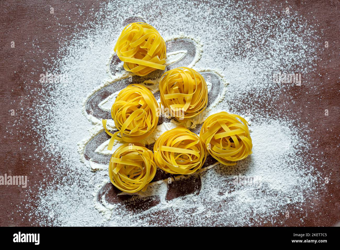Pâtes italiennes jaunes crues (nids) pappardelle, fettuccine ou tagliatelle en forme d'arbre de Noël sur fond marron, gros plan. Œuf fait maison Banque D'Images