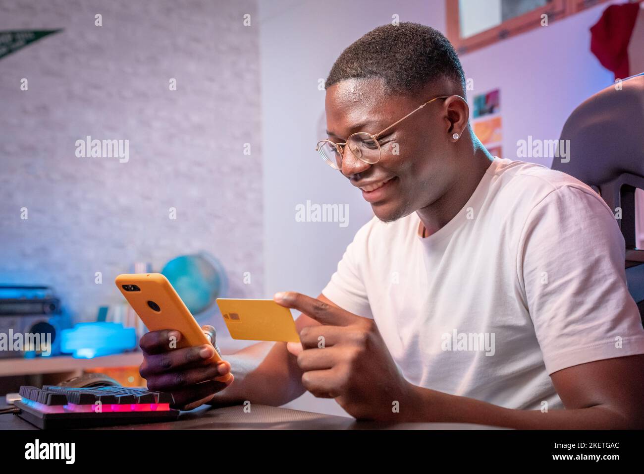 Jeune homme noir shopping en ligne sourire heureux tenant téléphone mobile et carte de crédit acheter et payer Banque D'Images