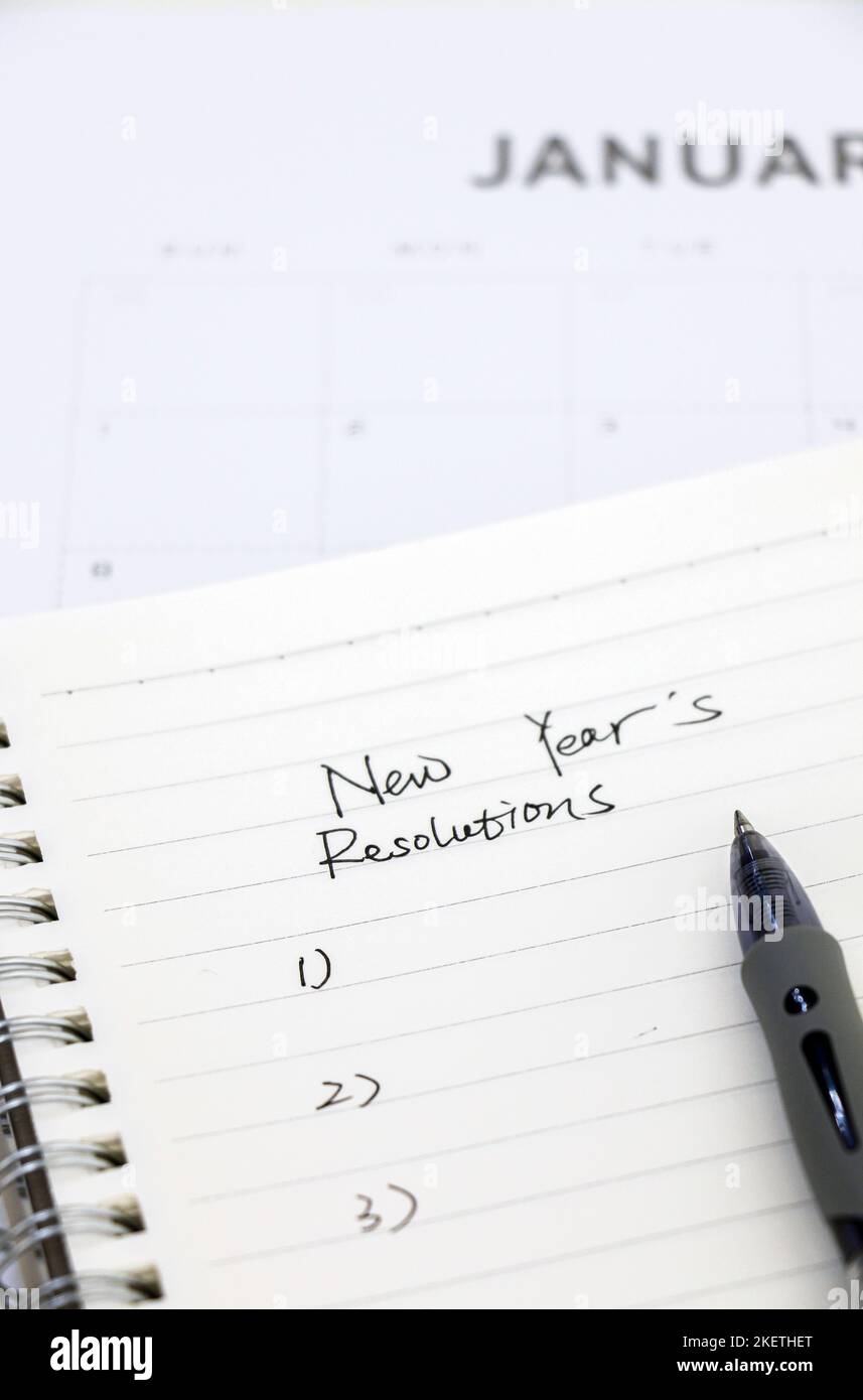 Bloc-notes avec la liste des résolutions du nouvel an et stylo à bille au premier plan en haut du calendrier de janvier en arrière-plan, sélection. Banque D'Images