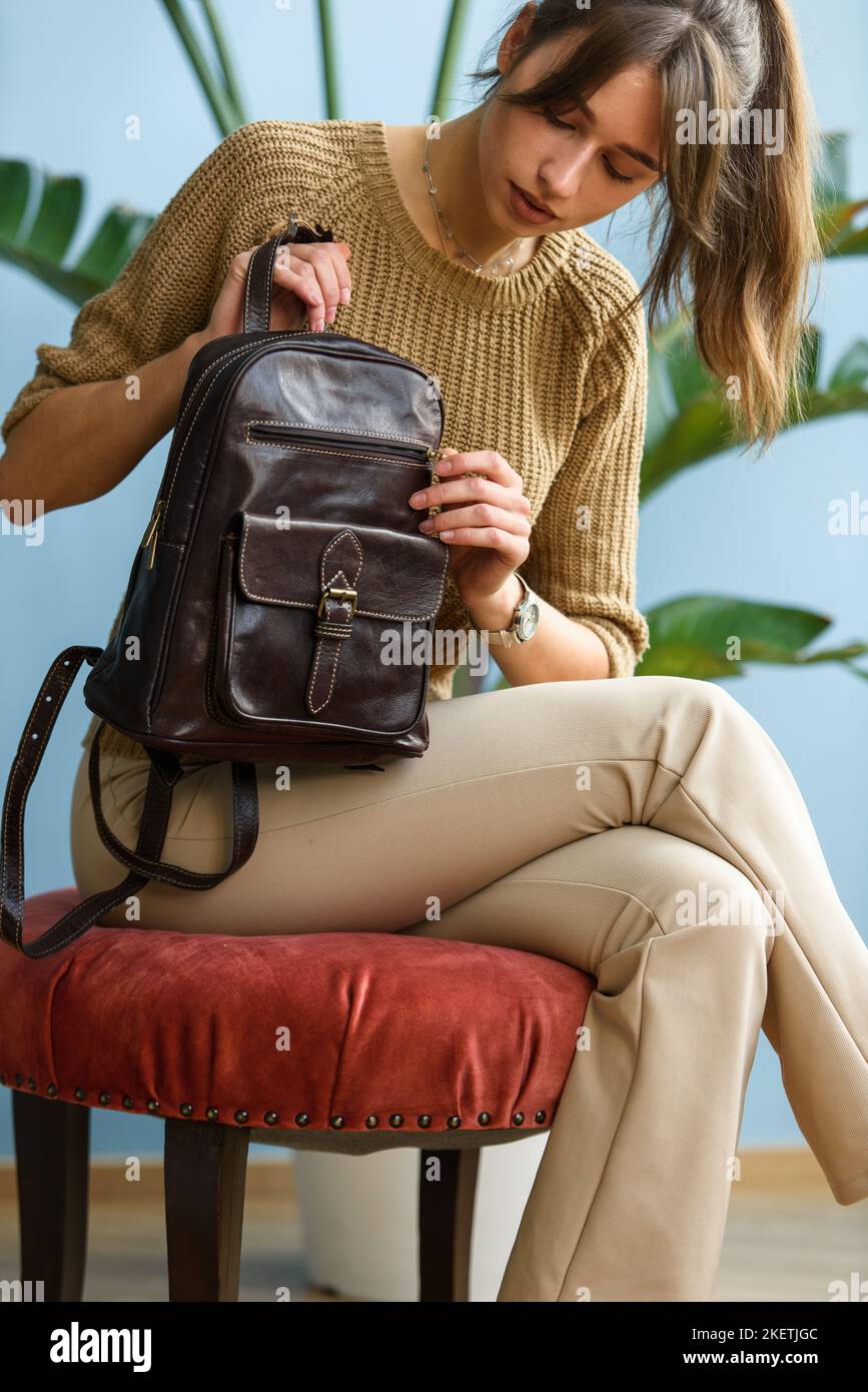 belle fille mince en pantalon beige et chandail olive posant tout en étant assis avec un petit sac à dos en cuir marron Banque D'Images