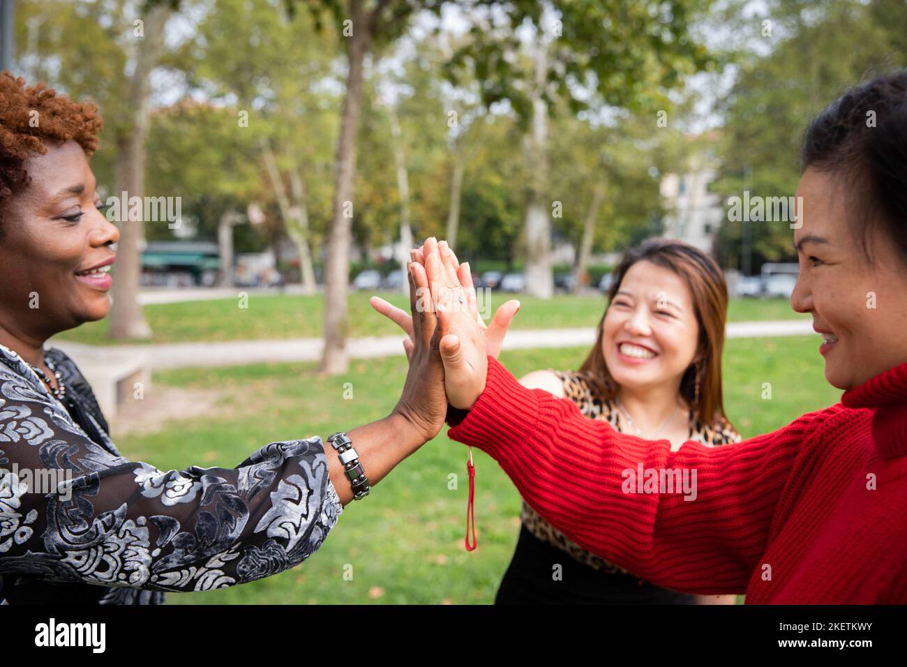 Trois femmes matures aux mains jointes souriantes dans un parc public Banque D'Images