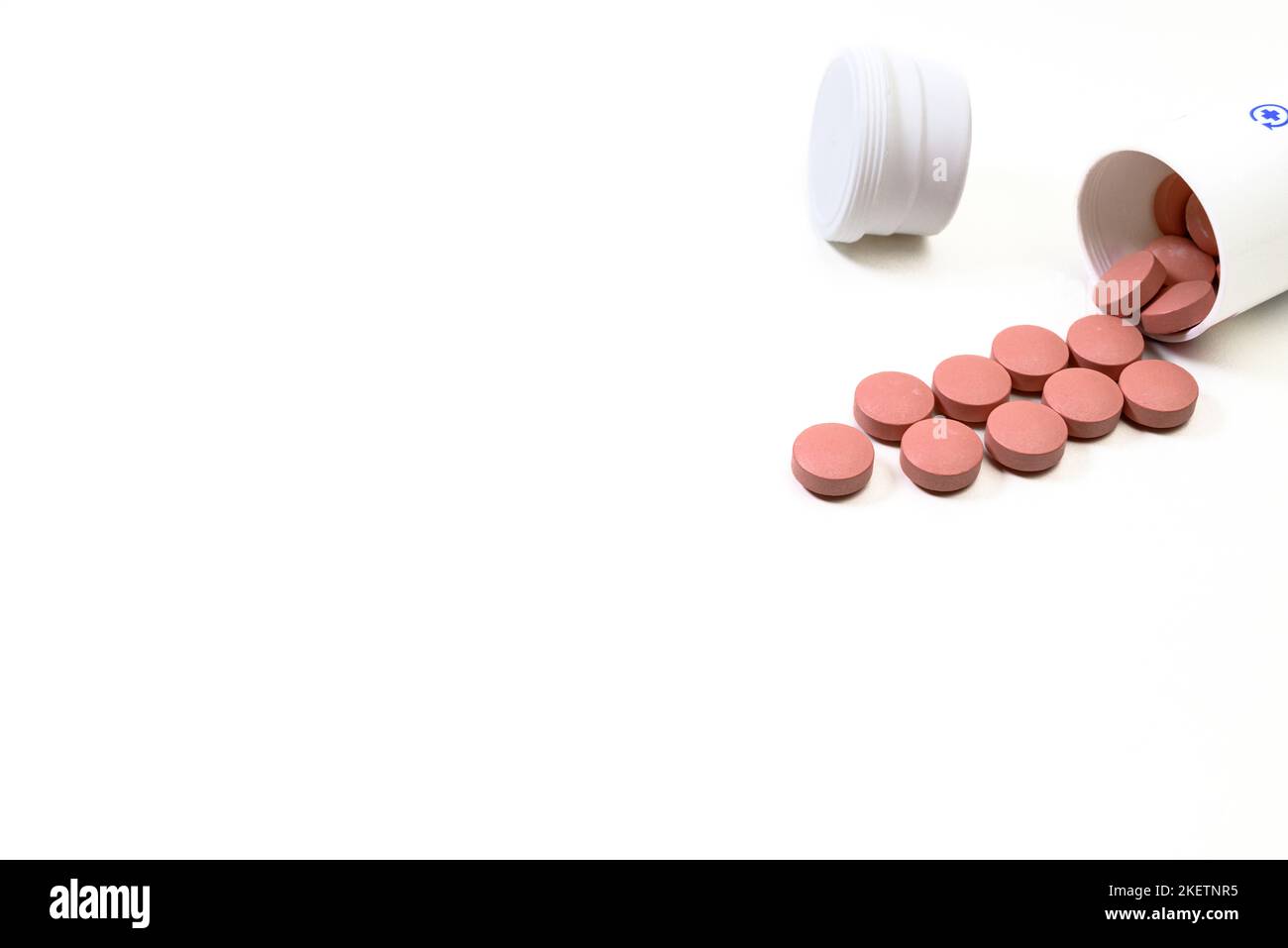 Des pilules de médecine rose débordent d'une bouteille blanche sur fond blanc Banque D'Images