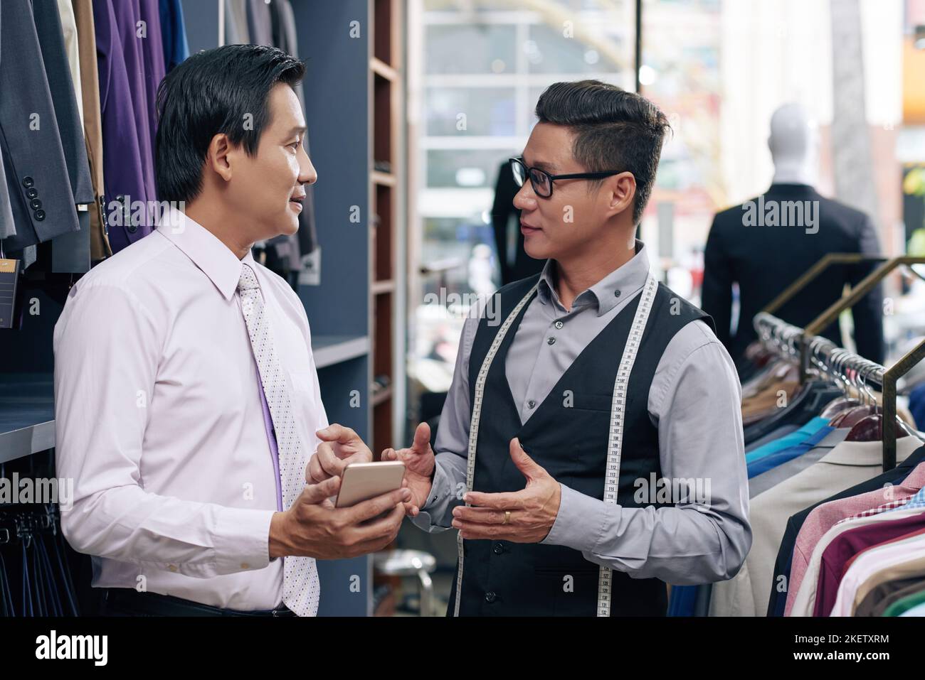 Un assistant d'atelier de vêtements pour hommes et un client discutent Banque D'Images