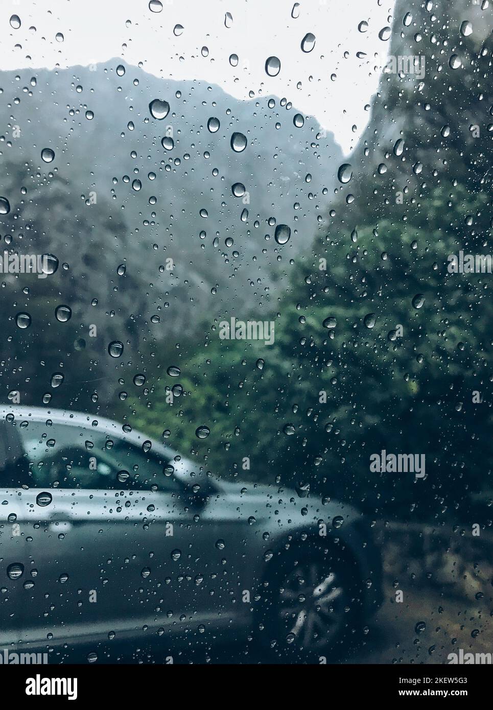 Gouttes de pluie sur l'image de verre de voiture propre avec voiture couleur argent sur l'arrière-plan. Automne profond froid pluie brouillard jour photo sur la place de stationnement de montagne. W Banque D'Images