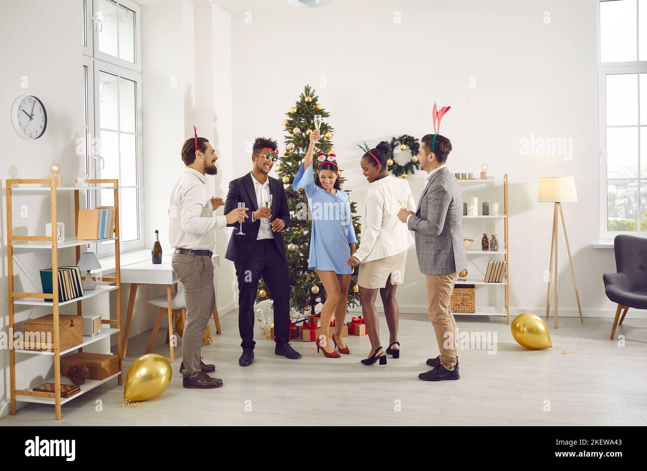 Des collègues dansent avec des verres de champagne lors d'une fête du nouvel an au bureau. Banque D'Images