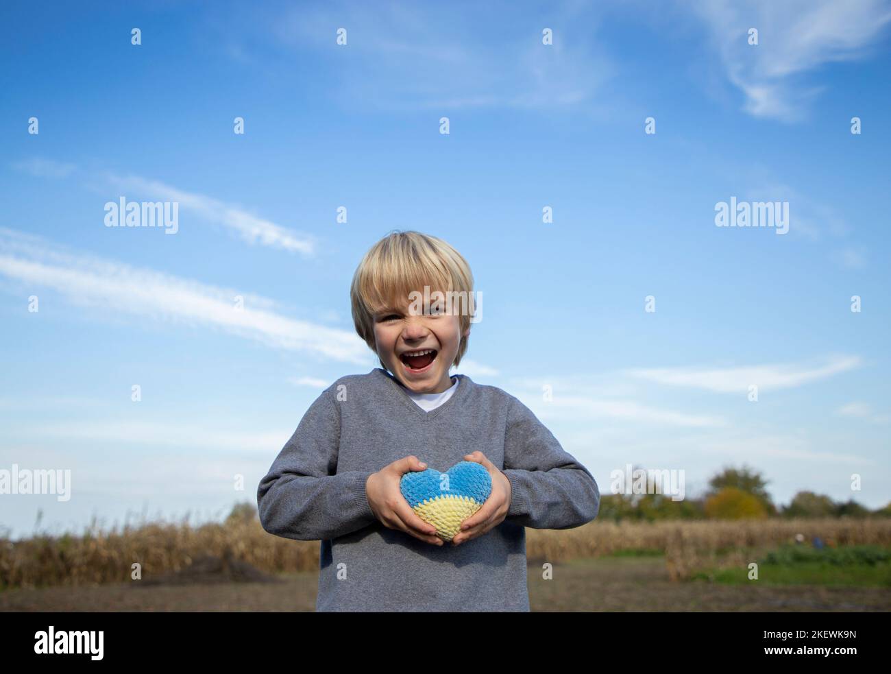 joyeux enfant heureux contre le ciel bleu, tenant un coeur tricoté jaune-bleu dans ses mains. Les enfants contre la guerre. Croyez en la victoire de l'Ukraine. Banque D'Images