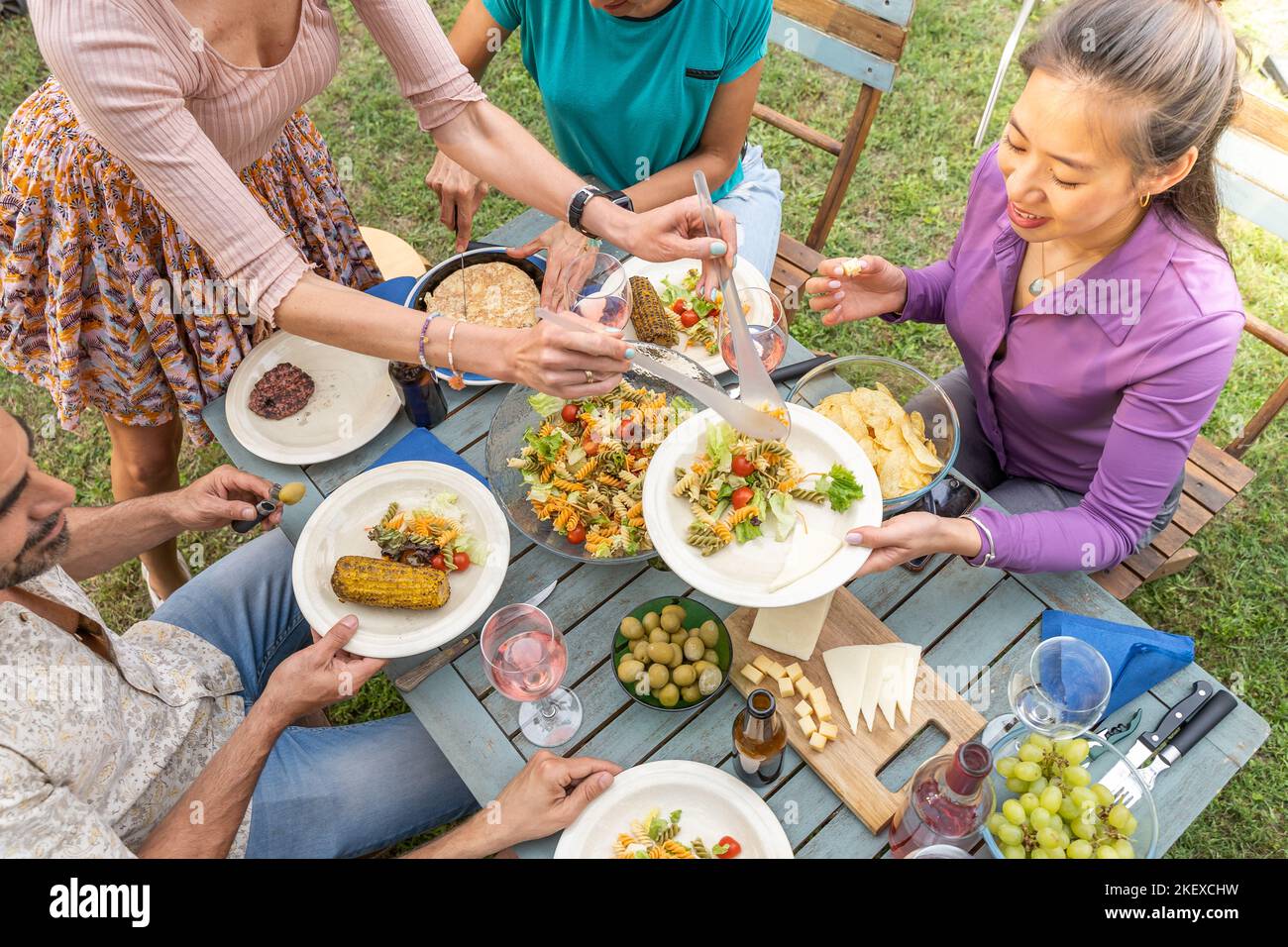 Amis multiculturels assis à une table en bois pour dîner. Ils ont des assiettes pleines de nourriture et des verres avec des boissons. Banque D'Images