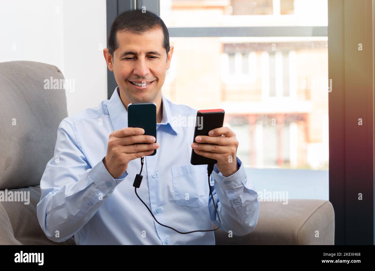 Happy man charge un smartphone avec un chargeur portable installé sur un canapé à la maison Banque D'Images