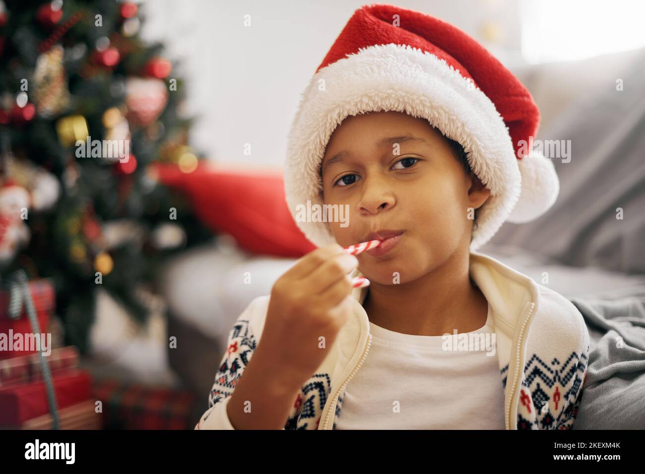 Gros plan sur un garçon afro-américain portant un chapeau de père Noël qui se réglisse de canne à sucre célébrant le Noël du nouvel an Banque D'Images