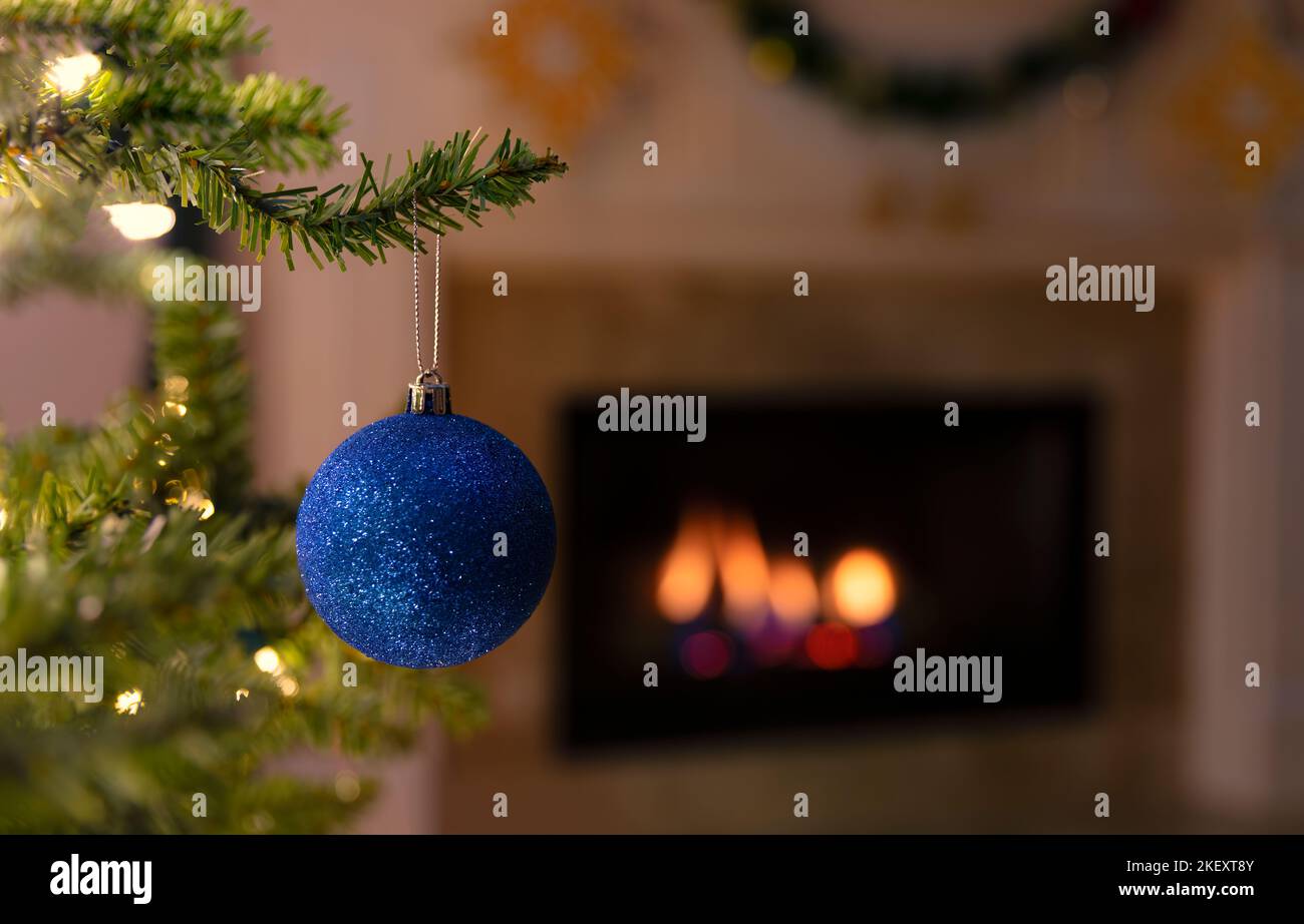 Gros plan d'un seul ornement bleu de Noël suspendu d'arbre avec cheminée en arrière-plan Banque D'Images