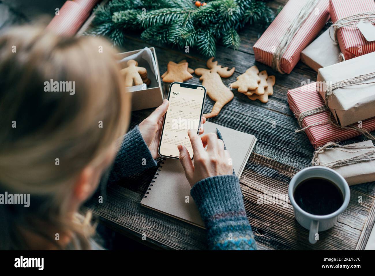 Femme prévoyant 2023 tenant un téléphone avec un calendrier sur l'écran de travail sur le bureau de noël Banque D'Images