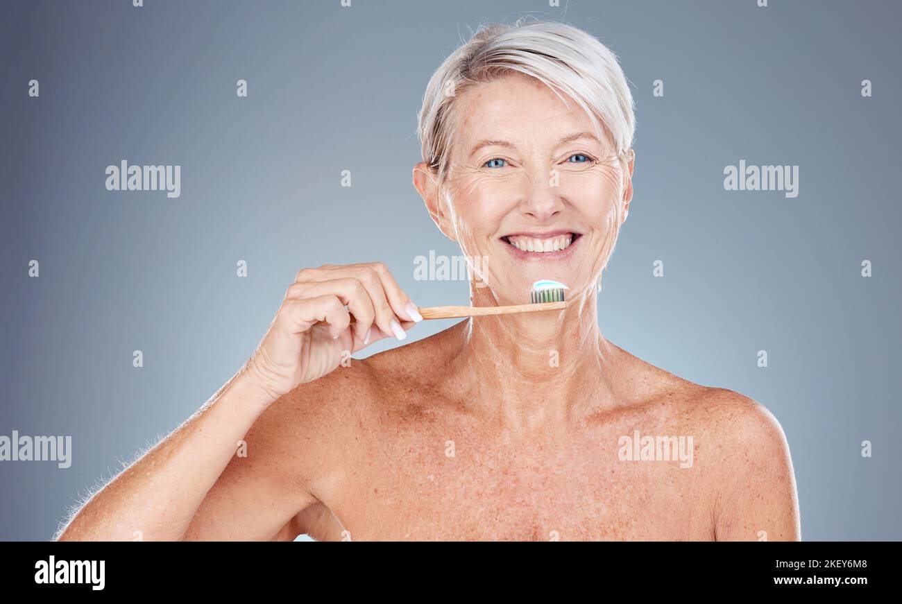 Dents, soins dentaires et femme mûre se brossant avec brosse à dents et dentifrice sur fond gris avec sourire sur le visage. Routine matinale, soins de santé Banque D'Images