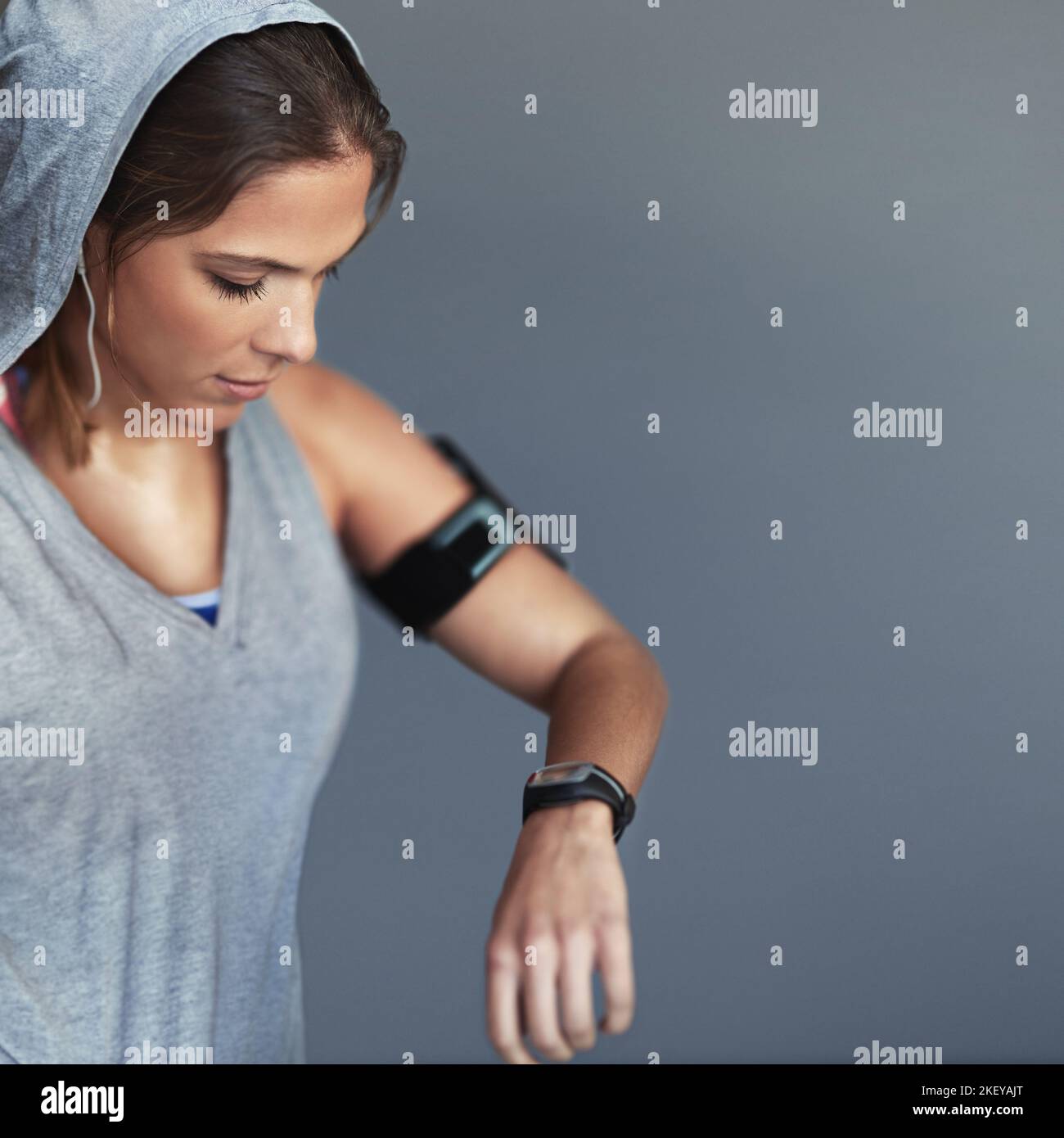 Un grand progrès. Une jeune femme sportive qui vérifie l'heure sur sa montre de sport sur fond gris. Banque D'Images